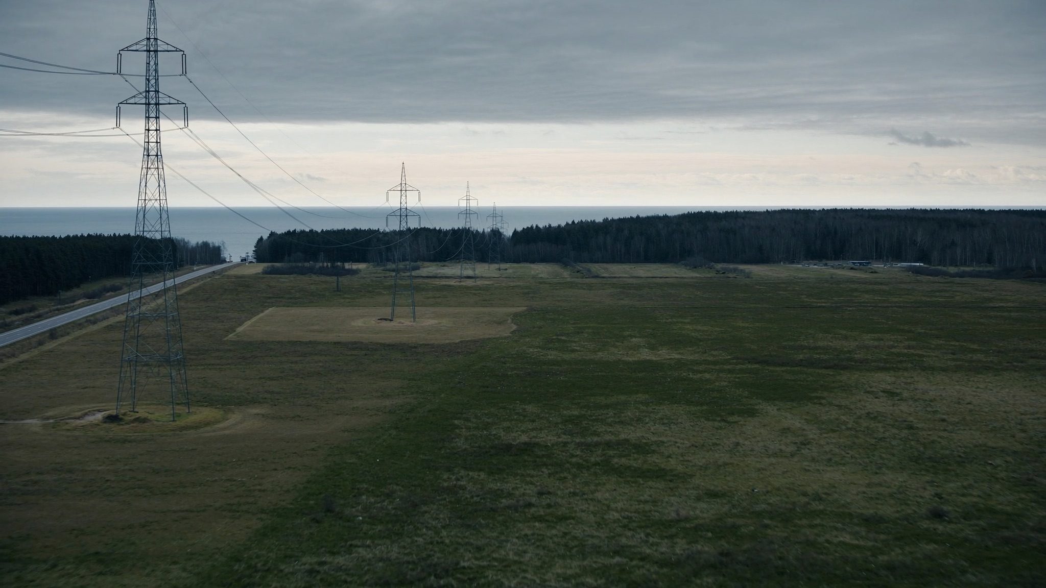 Illustrative view: high-voltage transmission lines crossing open greenfield land beside pine forest on Latvia’s Baltic coast