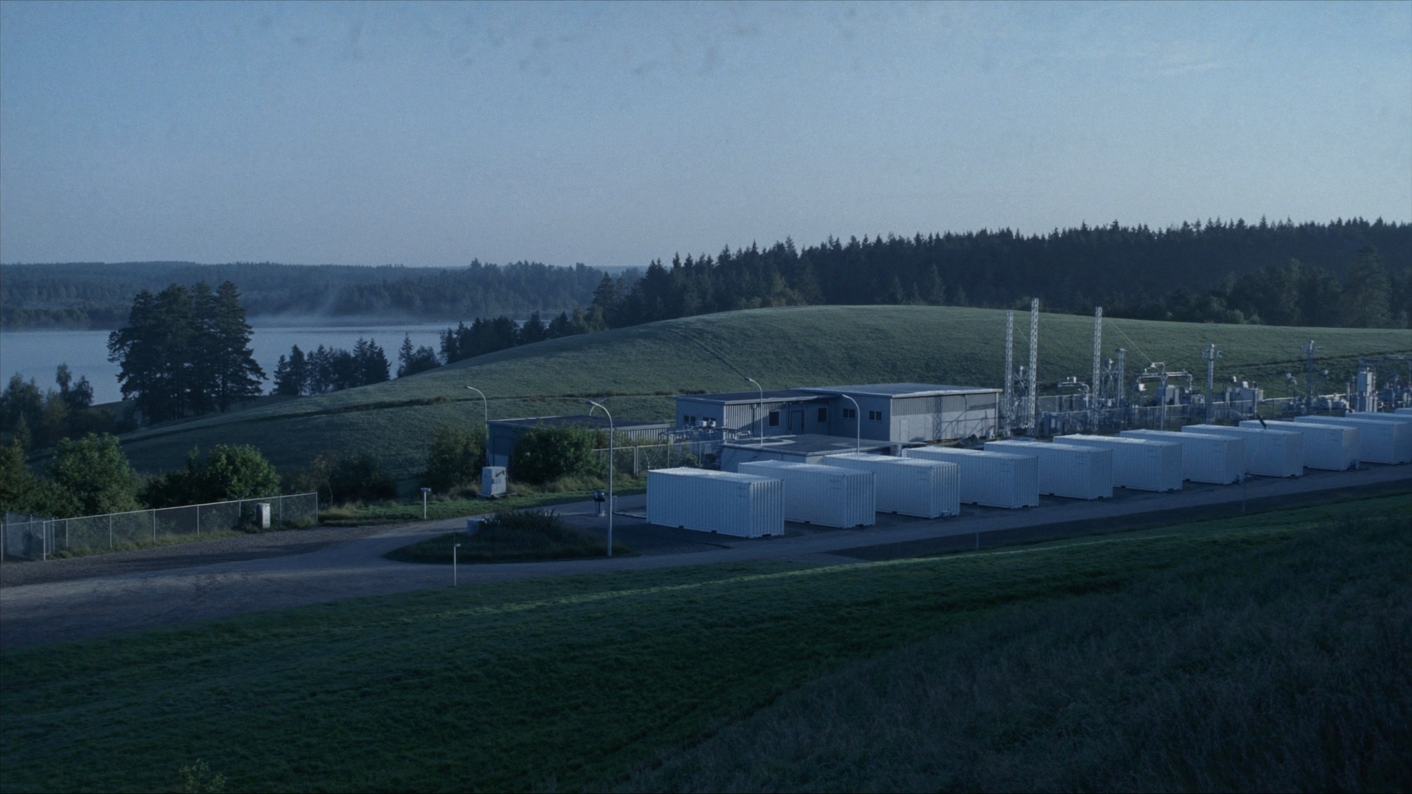 Illustrative view: battery storage containers beside a substation, with a misty lake and hills in eastern Latvia