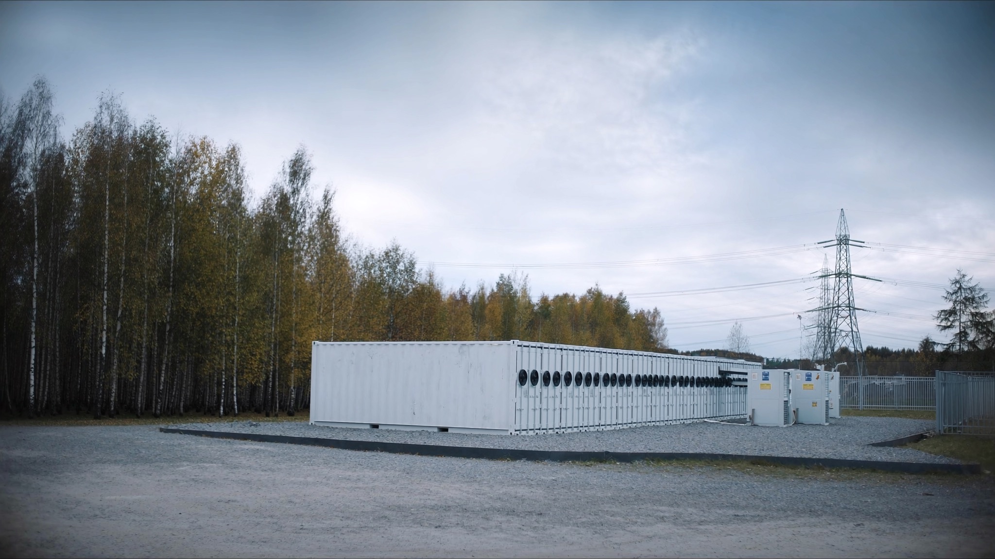 Illustrative view: battery storage containers beside high-voltage lines and birch forest in central Latvia